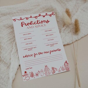 May include: A white card with red text and illustrations for a baby shower. The card reads "Predictions and Advice" with prompts for birth details and advice for the new parents. Festive illustrations include a snowman, Christmas tree, and house.