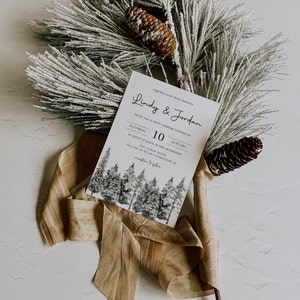 Puede incluir: Una invitaci&oacute;n de boda con una escena de bosque invernal. La invitaci&oacute;n es para Lindy & Jordan, y la boda es el s&aacute;bado 10 de enero a las 7:00 PM en The Cedar Room, 701 Bay St No 201, Charleston, SC.