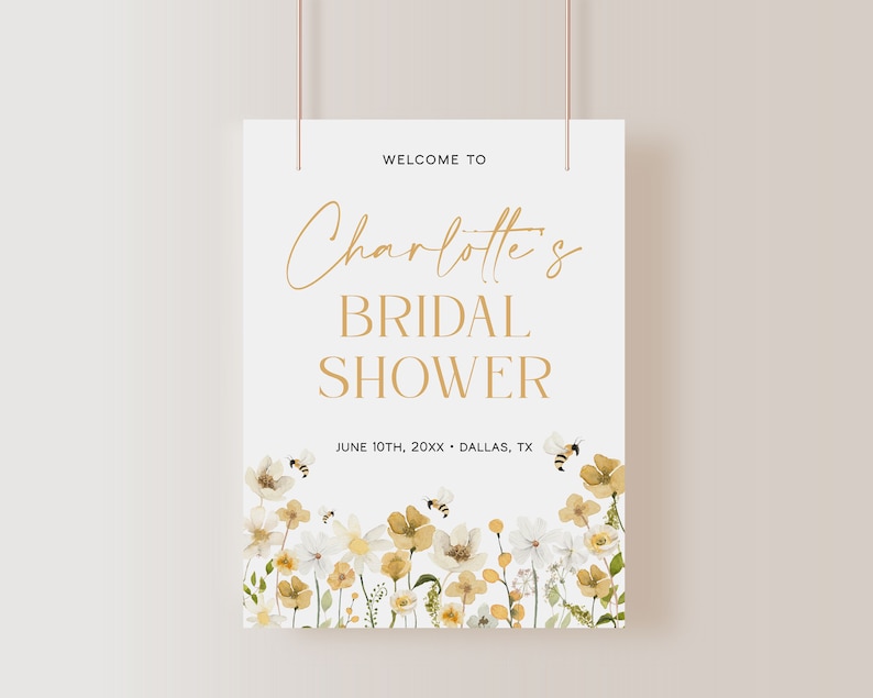 K&ouml;nnte beinhalten: Ein wei&szlig;es Brautdusche-Schild mit goldenen Buchstaben, auf dem "Willkommen zu Charlotte's Bridal Shower" und "June 10th, 20XX - Dallas, TX" steht. Das Schild ist mit einem Aquarell-Blumenrand aus wei&szlig;en und gelben Blumen und Bienen verziert.