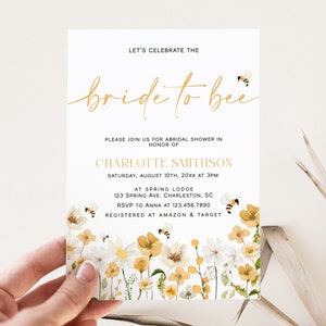Pu&ograve; includere: Un invito a una festa di addio al nubilato bianco con lettere dorate che recitano "Celebriamo la sposa". L'invito ha un bordo floreale con fiori gialli e bianchi e api.
