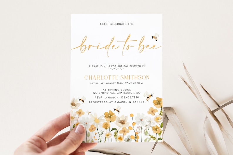 Pu&ograve; includere: Un invito a una festa di addio al nubilato bianco con lettere dorate che recitano "Celebriamo la sposa". L'invito ha un bordo floreale con fiori gialli e bianchi e api.
