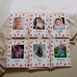May include: Six monthly milestone cards with a strawberry theme. Each card features a photo of a baby and the number of months. The cards are pink and white with a checkered pattern and red strawberries.