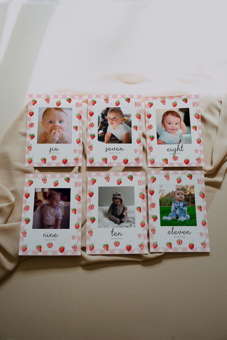 May include: Six monthly milestone cards with a strawberry theme. Each card features a photo of a baby and the number of months. The cards are pink and white with a checkered pattern and red strawberries.