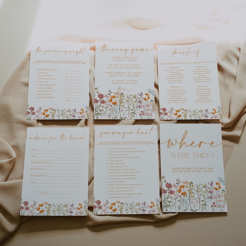 May include: A set of six bridal shower game cards with floral accents. The cards feature games like "The Price is Right," "The Ring Game," and "Drink If." The text is in a gold script font, and the cards have a white background.