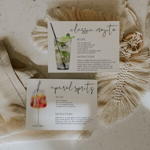 May include: Two recipe cards with watercolor illustrations of cocktails. The first card is for a classic mojito and the second card is for an Aperol spritz. Both cards have the ingredients and instructions for making the cocktails.