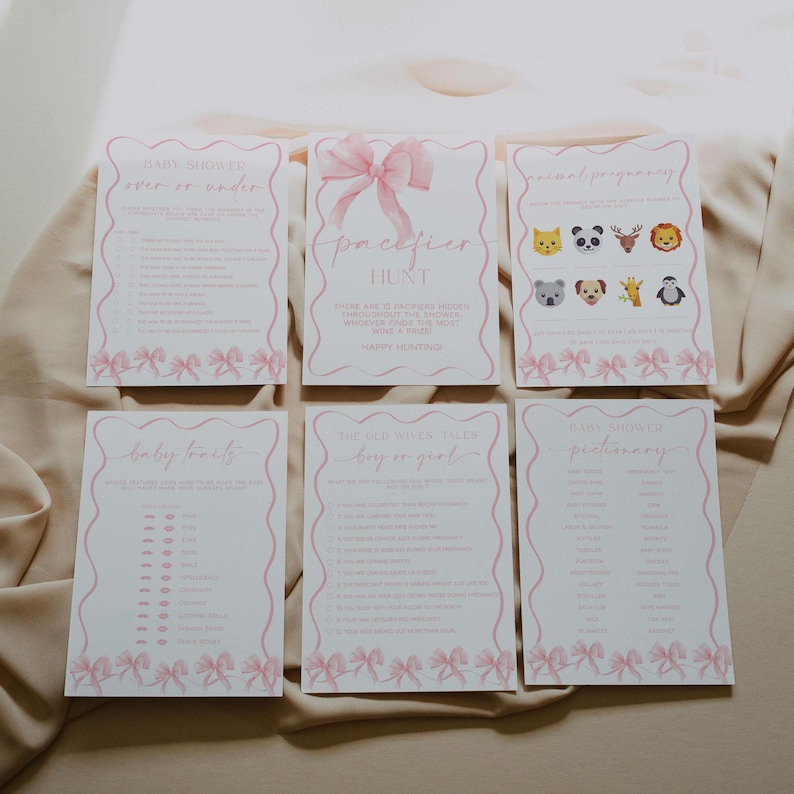May include: Six pink baby shower game cards with bow accents. The cards include games like "Over or Under," "Pacifier Hunt," and "Baby Traits." Each card has a pink bow design at the bottom and a pink border.