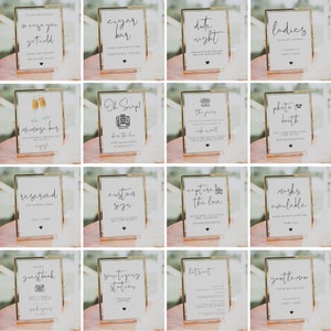 May include: A set of 16 gold-framed signs with white backgrounds and black text. The signs are for a wedding and include information such as "in case you get cold", "cigar bar", "date night", "ladies", "mimosa bar", "oh snap!", "the vows", "photo booth", "reserved", "custom sign", "capture the love", "masks available", "photo guestbook", "sanitizing station", "let's eat", and "gentlemen".