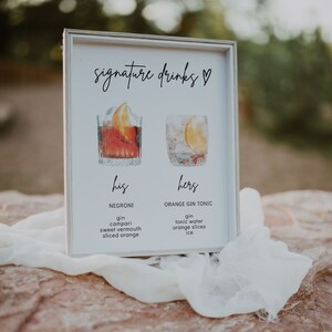 May include: A white sign with the text "signature drinks" in black cursive writing. The sign features two illustrations of cocktails, one red and one clear, with the text "his" and "hers" below each. The ingredients for each drink are listed below the illustrations.