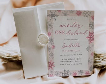 May include: A rectangular birthday invitation card featuring a border of pink and silver snowflakes. The text reads: join us in a winter ONEderland our little snowflake Isabella IS TURNING ONE saturday, january 10th at 4pm AT THE BROWN'S HOME 123 highland ave. | dallas, tx RSVP to Anna at 123.456.7890. A matching white envelope with a wax seal is included.