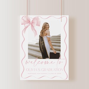 May include: A pink and white graduation welcome sign with a photo of a graduate in a cap and gown. The sign says "Welcome to Olivia's Graduation" and "Northside High School | Class of 20XX".