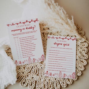 May include: Two white cards with red text and decorative elements. One card reads "Guess Who mommy or daddy?" and the other reads "Nursery rhyme quiz." Both cards are on a woven, beige surface.