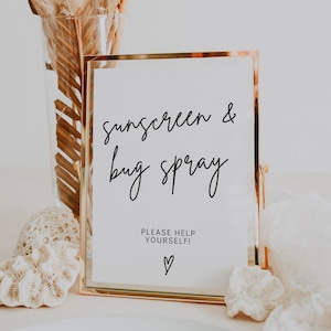 May include: A gold-framed sign with the text "Sunscreen & Bug Spray" and the words "Please Help Yourself!" with a heart symbol below.