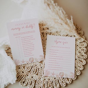 May include: Two rectangular paper game cards with pink text and seashell illustrations at the bottom. The left card is titled Guess Who mommy or daddy? and the right card is titled Nursery rhyme quiz. Both cards feature lists of questions.