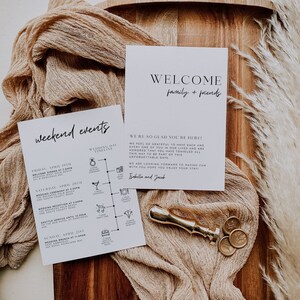 May include: A white card with black text that says "Weekend Events" and lists a schedule of events for a wedding weekend. The card also includes a welcome message that says "Welcome family + friends" and "We're so glad you're here!"