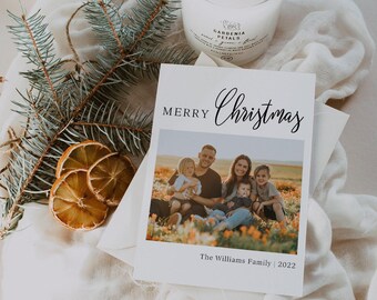 May include: A white rectangular Christmas greeting card featuring the text Merry Christmas and a photograph of a family of five sitting in a field of orange flowers. The card includes the text The Williams Family | 2022 at the bottom.