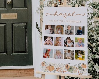 May include: A white sign with a brown border and the name "hazel" written in cursive. The sign has a collage of photos of a baby girl at different ages, with the text "My First Year - October 2024" below the name. The sign is decorated with a border of fall-themed pumpkins and leaves.