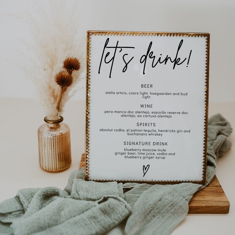 May include: A white sign with a gold frame and the text "let's drink!"  The sign lists different types of beer, wine, spirits, and a signature drink: blueberry moscow mule.