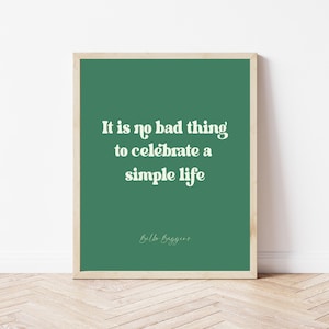 May include: A green framed print with a white quote that reads "It is no bad thing to celebrate a simple life" and the name "Ella Baggins" at the bottom.