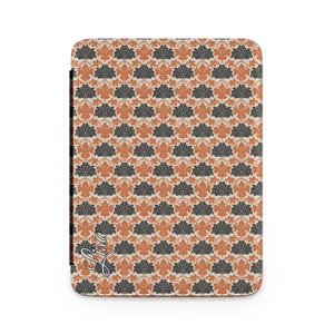 Puede incluir: Una funda rectangular con un patrón floral repetido en tonos naranja, gris y crema. El diseño presenta hojas estilizadas. El nombre "Lisa" está escrito en cursiva en la esquina inferior izquierda.