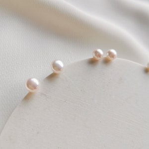 May include: A close-up of four white pearl earrings on a white surface. The pearls are round and smooth.