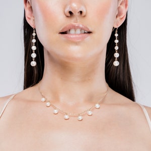 May include: A gold necklace and matching earrings with white pearls. The necklace has a delicate chain with pearls dangling from it. The earrings are long and feature a row of pearls.