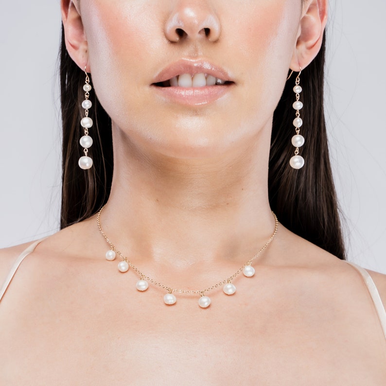 May include: A gold necklace and matching earrings with white pearls. The necklace has a delicate chain with pearls dangling from it. The earrings are long and feature a row of pearls.