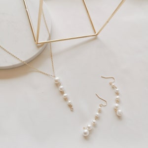 May include: A set of gold pearl jewelry featuring a necklace and earrings. The necklace and earrings each have a chain with a row of pearls hanging from it.
