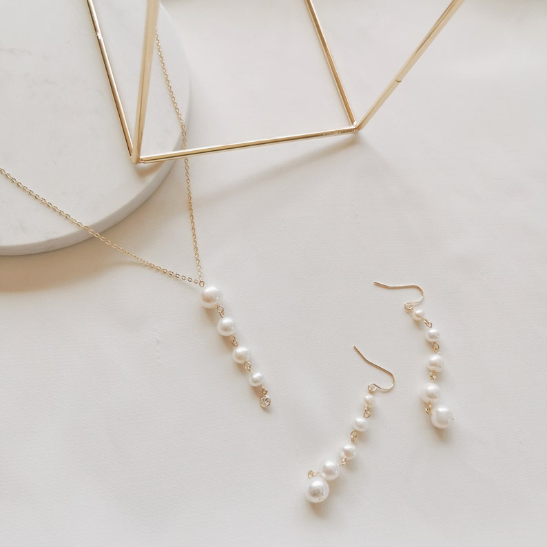 May include: A set of gold pearl jewelry featuring a necklace and earrings. The necklace and earrings each have a chain with a row of pearls hanging from it.