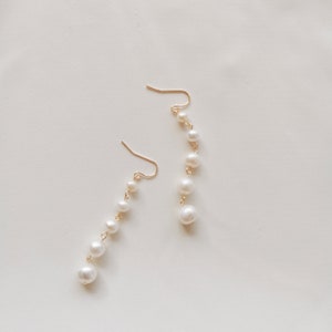 May include: A pair of gold earrings with a dangling chain of white pearls.