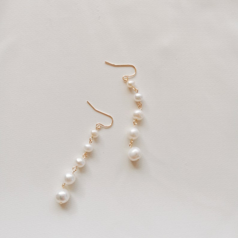 May include: A pair of gold earrings with a dangling chain of white pearls.