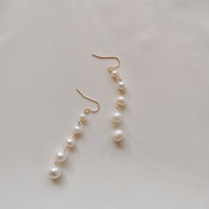 May include: A pair of gold earrings with a dangling chain of white pearls.