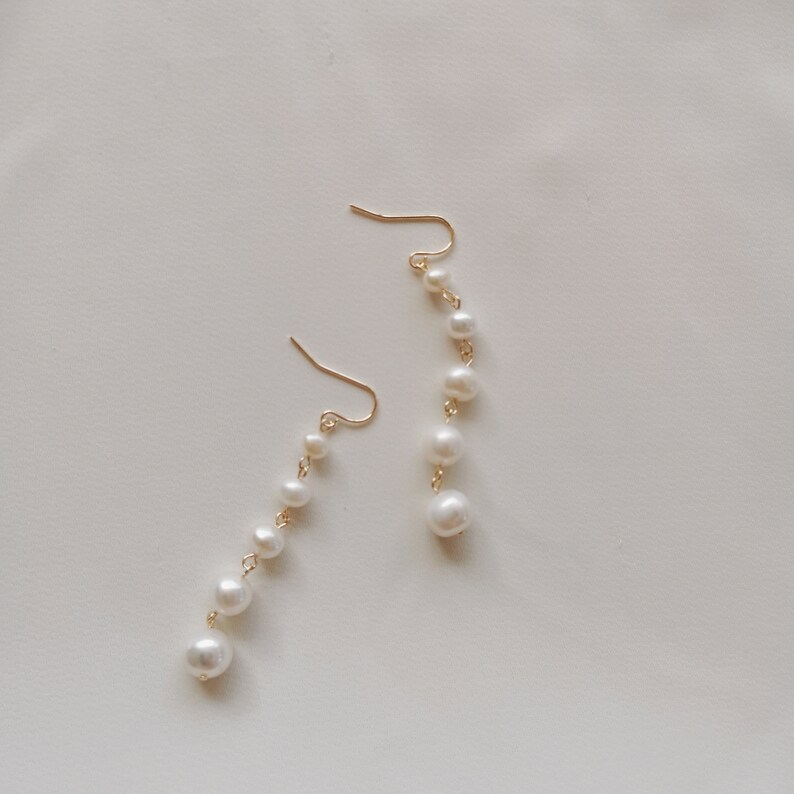 May include: A pair of gold earrings with a dangling chain of white pearls.