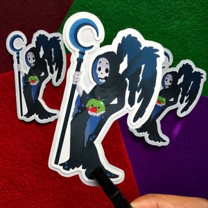 May include: Three black and blue stickers of a skeleton figure with wings holding a staff with a crescent moon on top and a green apple. The figure is wearing a black robe and has a skull face.