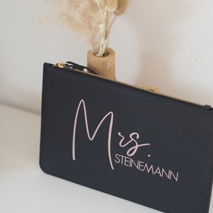 Pode incluir: Bolsa preta com z&iacute;per com o texto "Mrs. STEINEMANN" em escrita rosa.