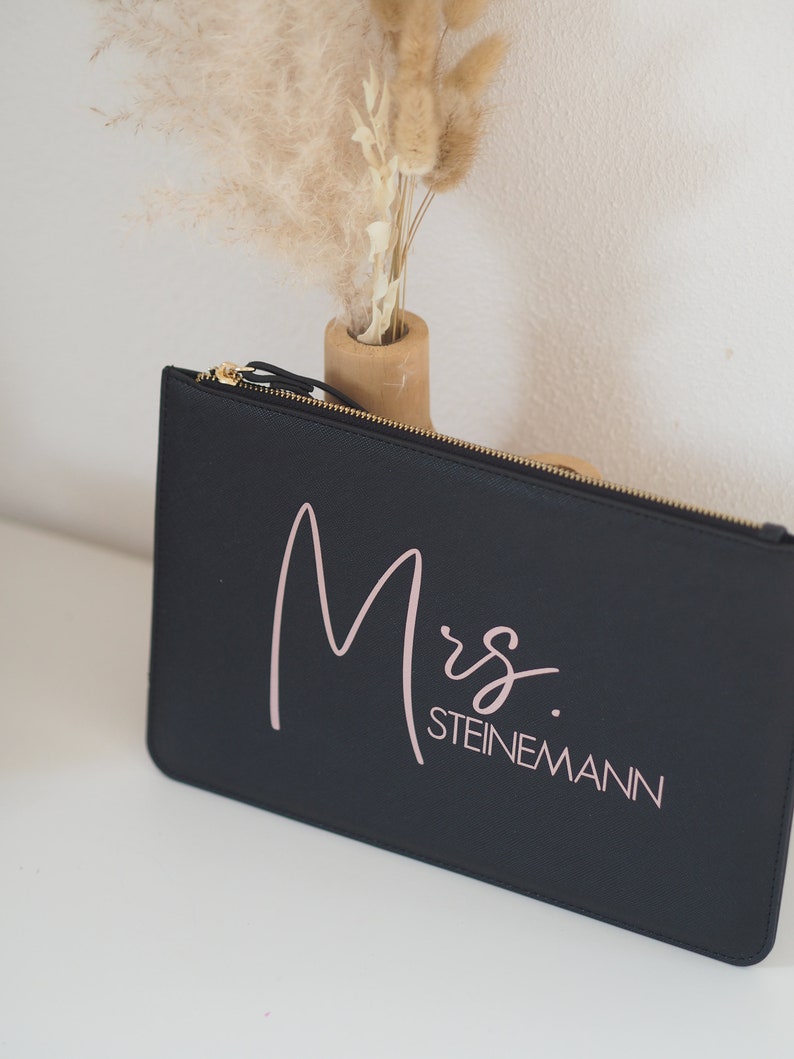 Pode incluir: Bolsa preta com z&iacute;per com o texto "Mrs. STEINEMANN" em escrita rosa.