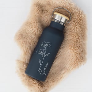 Può includere: Una bottiglia d'acqua in acciaio inossidabile blu scuro con un tappo in legno e un design floreale bianco. La bottiglia ha la scritta "Summer".
