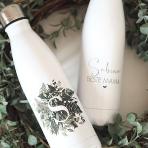 Puede incluir: Dos botellas de agua de acero inoxidable blancas con texto personalizado. Una botella tiene un diseño de hojas verdes con la letra "S" en el centro. La otra botella tiene el texto "Sabine Beste Mama" con un pequeño corazón.