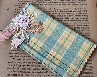 May include: A close-up of a book page with text about Wadi Sudr, a dry riverbed in the desert. The text describes the landscape as being white and barren, with steep sides and a gleaming white wadi. The page is partially covered by a piece of fabric with a blue and yellow plaid pattern.