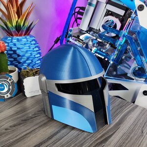 May include: A blue and white 3D printed helmet with a visor. The helmet is sitting on a wooden table.