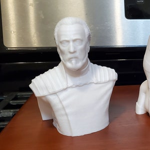 May include: Three white 3D printed busts of characters from the Star Wars franchise. The bust on the left is of a man with a beard and a long robe. The bust in the middle is of a woman with long hair and a headpiece. The bust on the right is of a character wearing a helmet and holding a blaster.