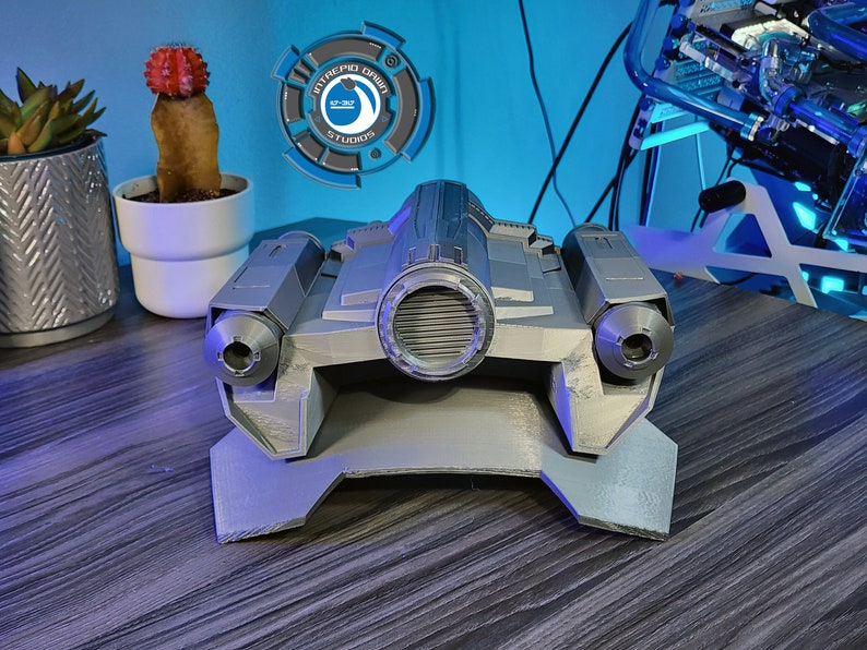 May include: A silver-colored, 3D printed model of a spaceship with two exhaust ports on the back and a large, round engine in the center.