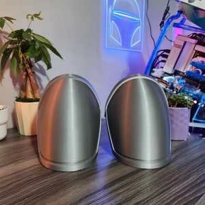 Pu&ograve; includere: Due oggetti arrotondati di colore argento, simili a caschi, con una finitura liscia e metallica. Gli oggetti sono posizionati su una superficie di legno.