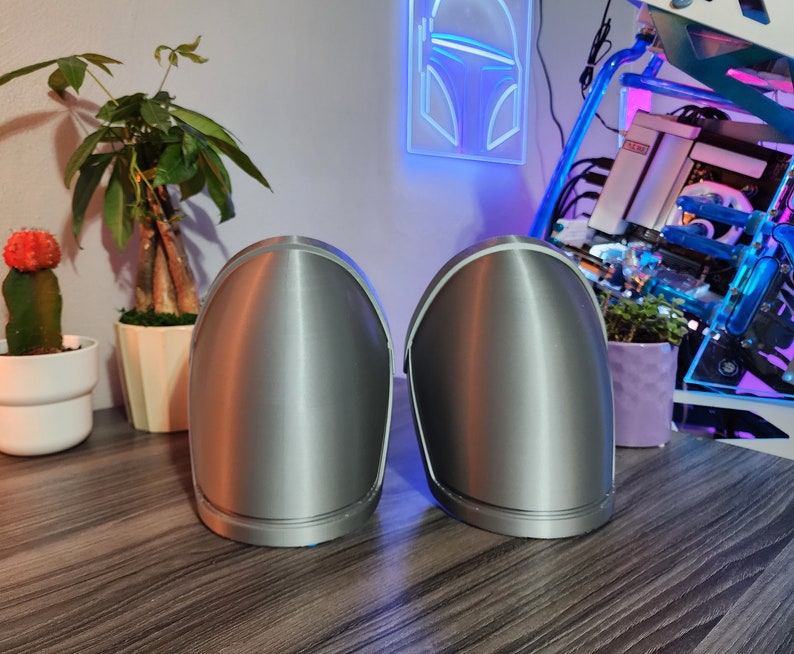 Pu&ograve; includere: Due oggetti arrotondati di colore argento, simili a caschi, con una finitura liscia e metallica. Gli oggetti sono posizionati su una superficie di legno.