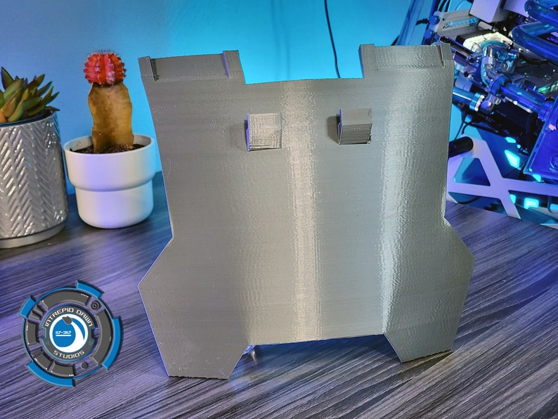 May include: A gray 3D printed plastic part with two rectangular cutouts. The part is sitting on a wooden surface.