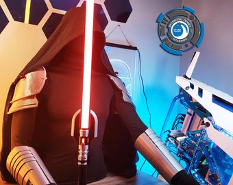 Op de afbeelding: Een gekapte figuur met een rood lichtzwaard, die een zilveren harnas en een zwarte mantel draagt, zit voor een witte computerbehuizing met blauwe lichten. De computerbehuizing heeft een logo met de tekst "Intrepid Origin Studios".