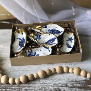 May include: Set of six blue and white oyster shell ornaments with gold accents. Each ornament features a different sea creature, including a turtle, a whale, a starfish, and a seahorse. The ornaments are packaged in a brown box with a white label that says "Small".