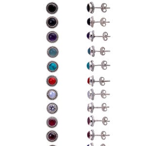 Può includere: Una collezione di orecchini a bottone con varie pietre preziose colorate. Ogni orecchino presenta una gemma rotonda incastonata in una lunetta argentata con texture a corda. I colori delle pietre preziose includono verde, nero, viola, blu, rosso e bianco.