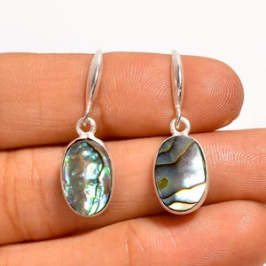 May include: A pair of silver drop earrings featuring oval abalone shell inlays. The iridescent shells show green, blue, and silver hues. The earrings have a simple, elegant design, suitable for everyday wear.