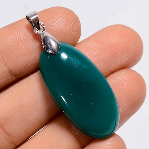 May include: A polished, oval-shaped pendant with a deep teal green gemstone. The pendant has a silver-colored metal bail for attaching to a chain. The gemstone is smooth and reflects light.