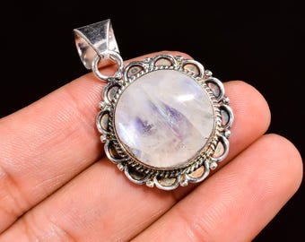 May include: A round, silver-toned pendant with a large, iridescent, moonstone center. The moonstone has a milky white base with subtle blue and purple flashes. The pendant is surrounded by a decorative, scalloped frame.